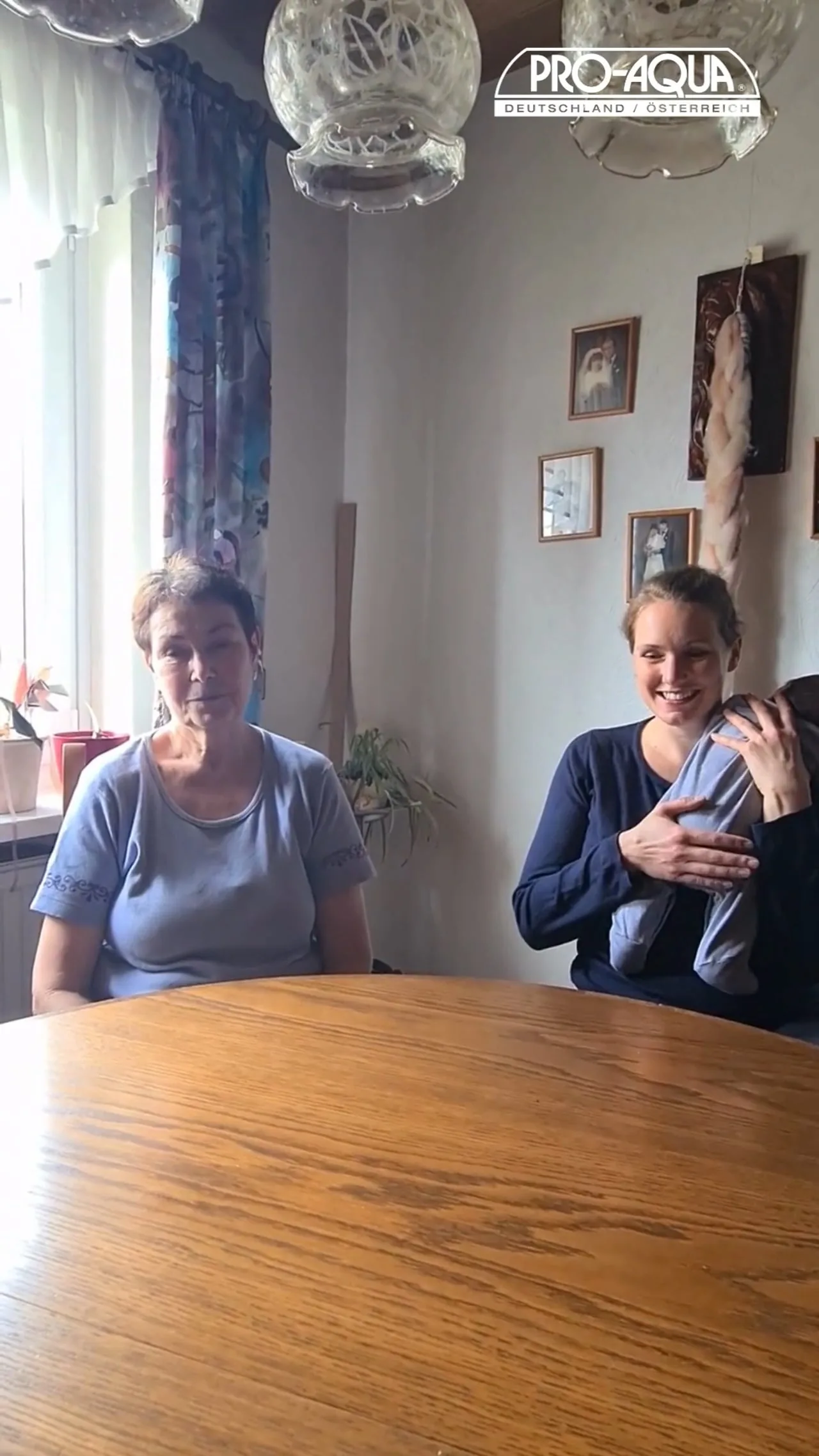 Videovorschau: Erika und Christina sitzen an einem Esstisch im Wohnzimmer, Christina hält ihr Baby auf dem Arm